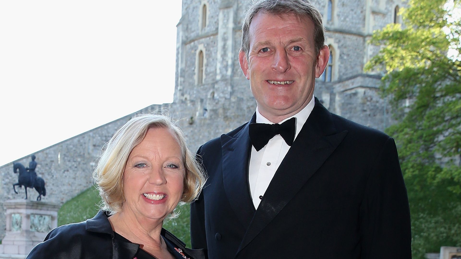 Deborah Meaden in red heels posing outside for a photo with her husband Paul