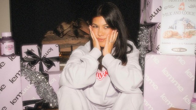 Kourtney Kardashian sitting on the ground in sweat pants surrounded by Christmas presents and tinsel