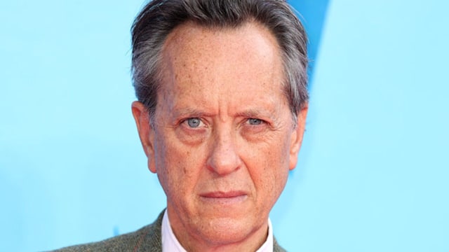 Close up of Richard E. Grant wearing a green suit. 