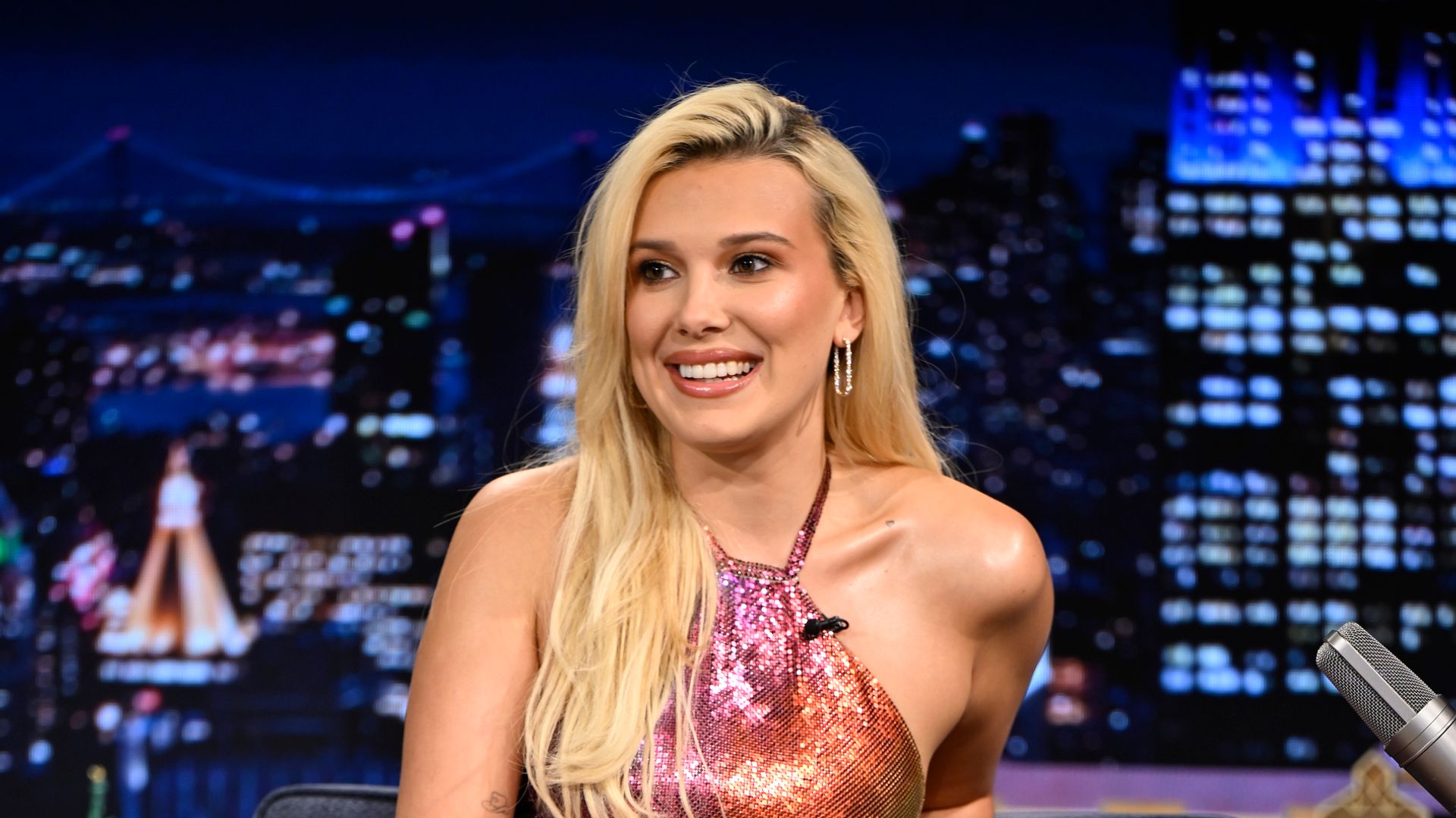 Millie Bobby Brown bronze dress blonde hair sitting down