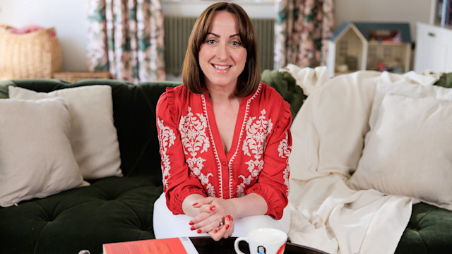 Natalie Cassidy smiling on the sofa in a red top with a cup of tea