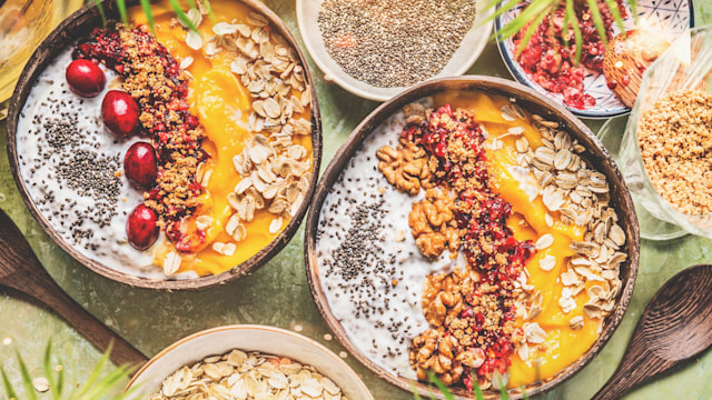 stock image of smoothie mango bowls with chia seeds yogurt pudding and cranberries, nuts, oatmeal topping in coconut shells with spoon, top view