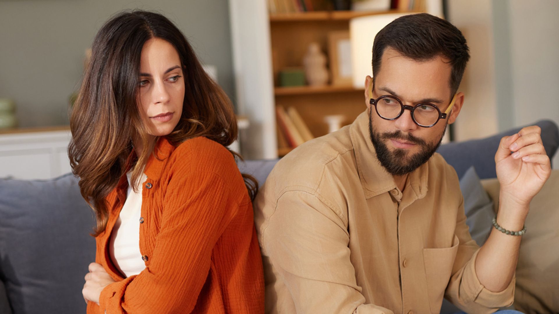 Couple sitting back-to-back on a sofa looking angry and upset 