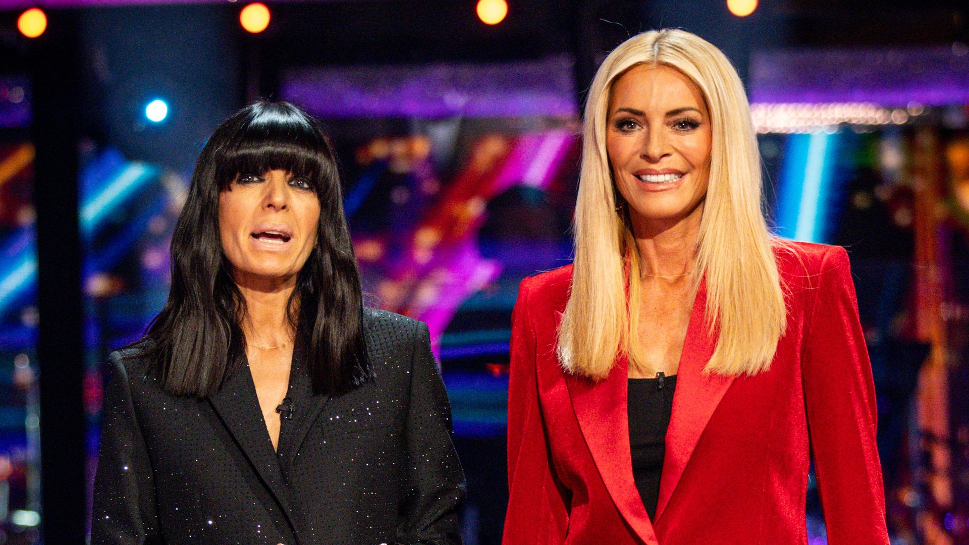 Claudia Winkleman in black standing with Tess Daly in a red velvet suit