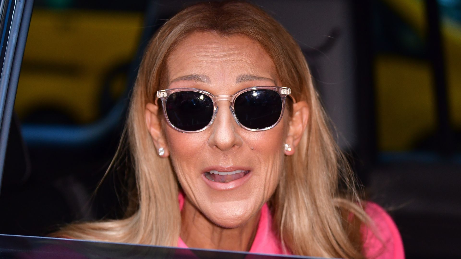 Celine Dion wearing sunglasses and a pink outfit in the back of a car in 2020