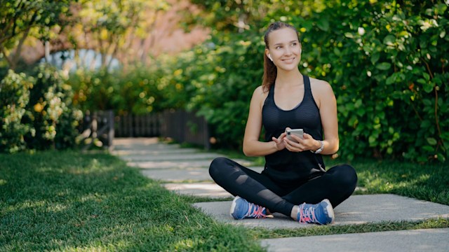 Sportswoman sits crossed legs outdoors checks newsfeed via smartphone