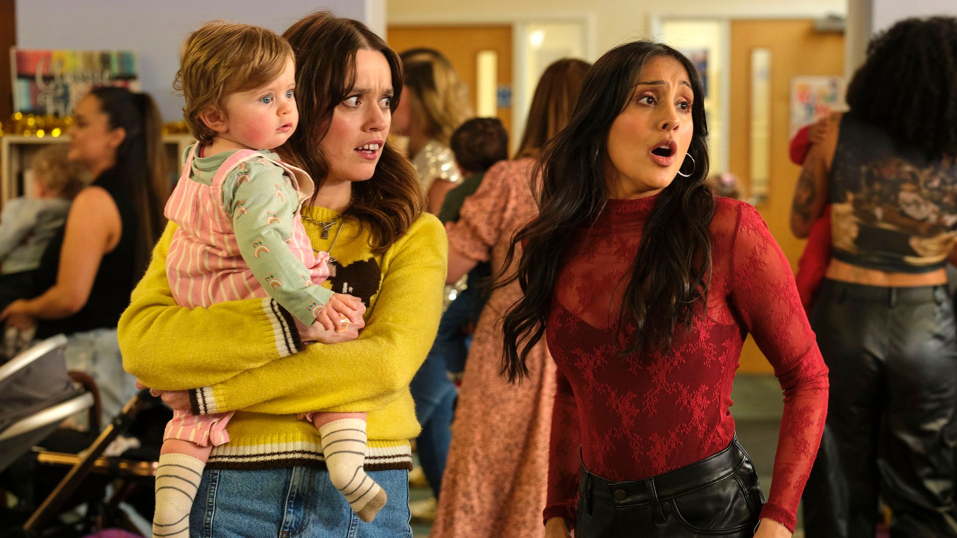 woman holding baby next to another woman in crowded room 