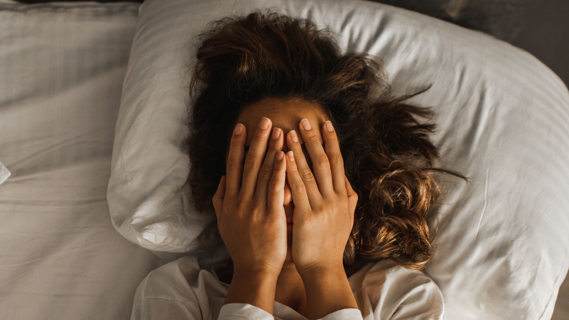 woman in bed with hands on eyes 
