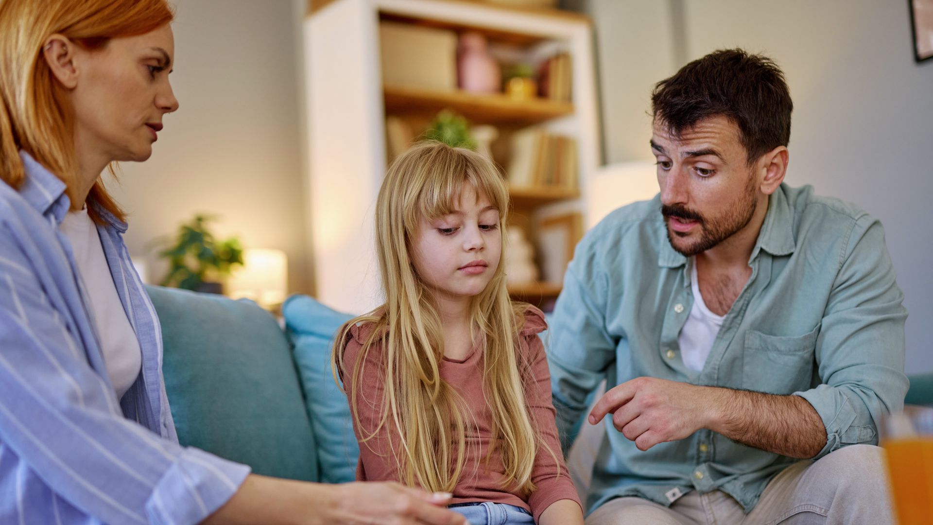 Parents sitting on the sofa in the living room, discussing their daughter's recent mistake while she listens with a sad expression. Tension fills the air as they address her behavior