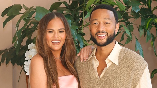 Chrissy Teigen and John Legend smiling against plants