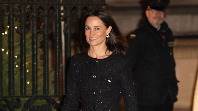 Pippa Middleton smiles outside at night, wearing the same chic black tweed dress with sparkling detail, red heels, and a red clutch, framed by festive Christmas lights.