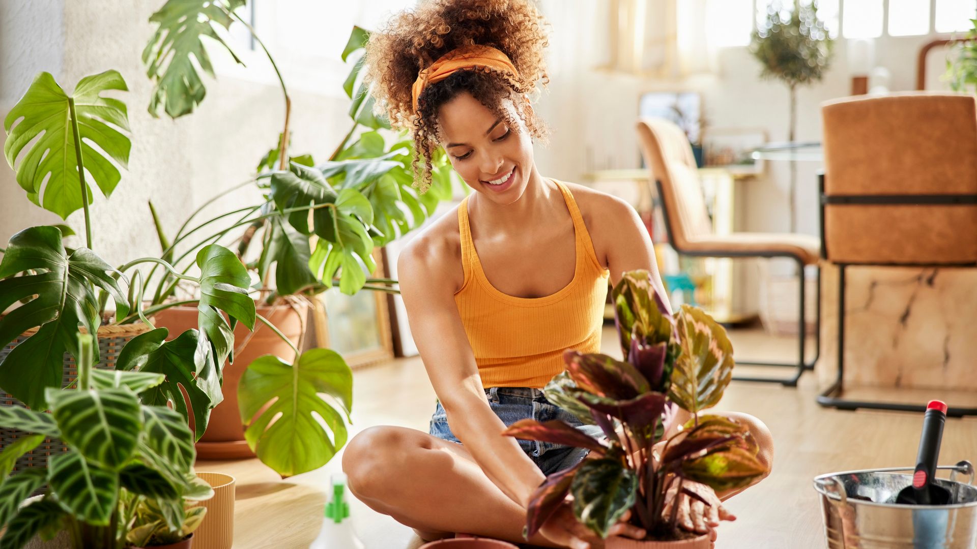 Smiling woman planting while sitting cross legged by potted plants. Young woman is wearing casuals. She is in living room at home.