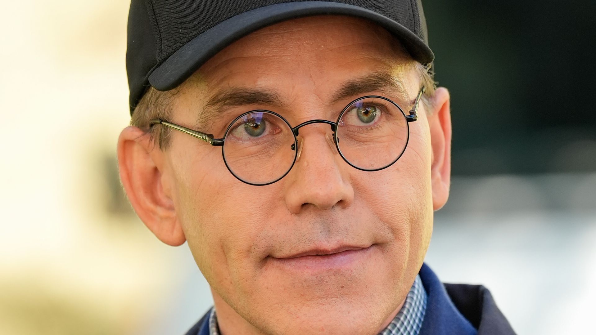 Close-up of man in navy jacket wearing glasses and 'ncis' cap