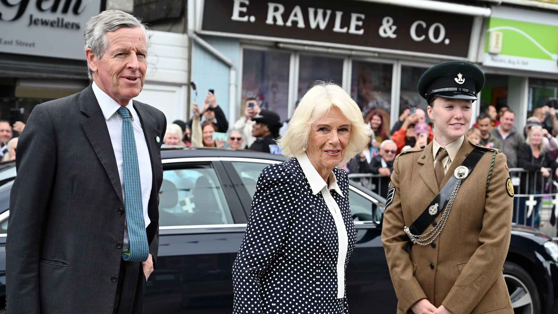 Queen Camilla standing with a man in a suit and a lady in military uniform