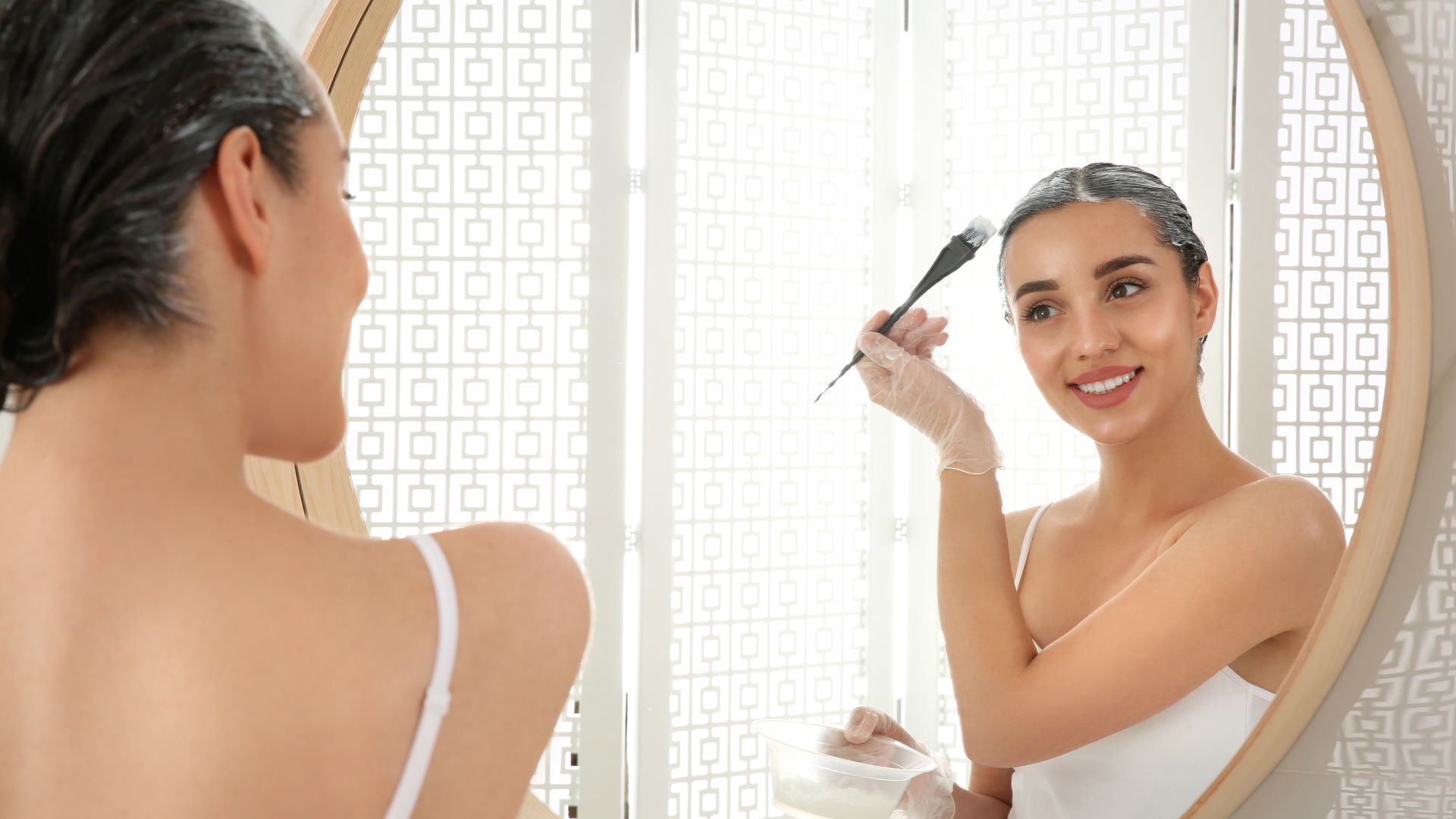 Young woman applying dye on hairs near mirror indoors