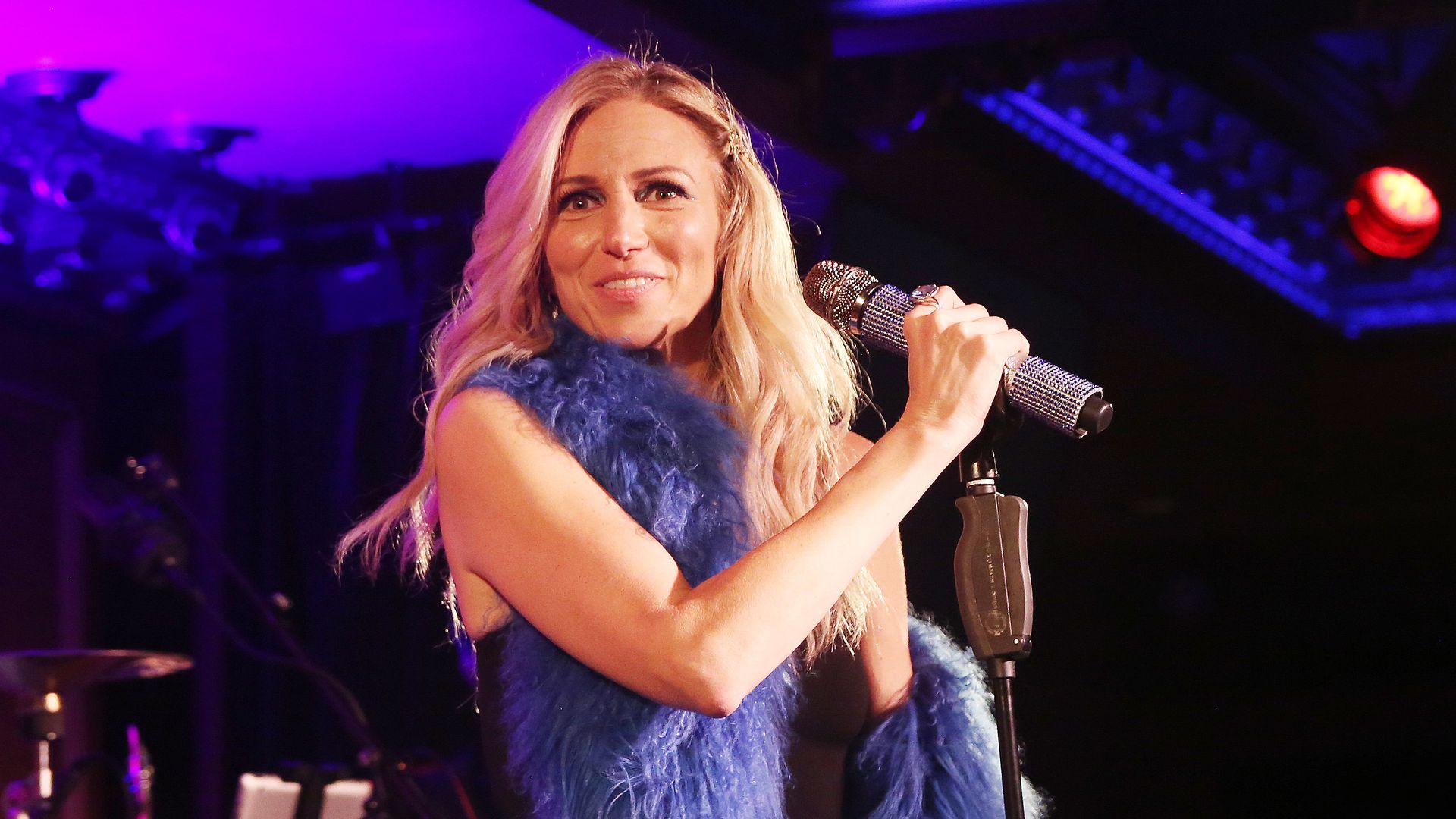 Debbie Gibson stands out in blue feather boa and holds the microphone