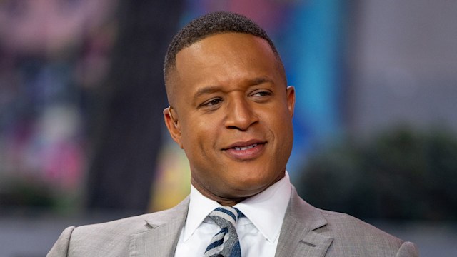 TV host in grey suit sitting on sofa in studio