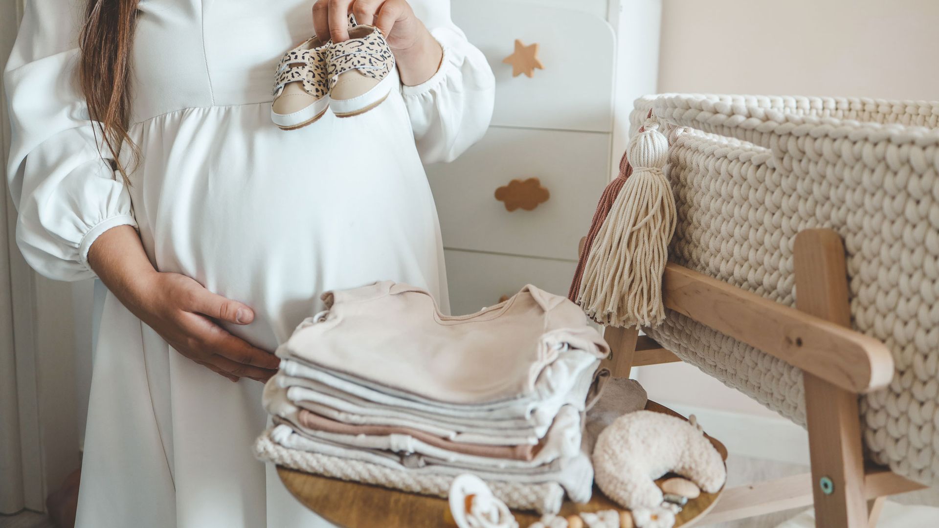Pregnant woman in white dress prepping nursery for newborn