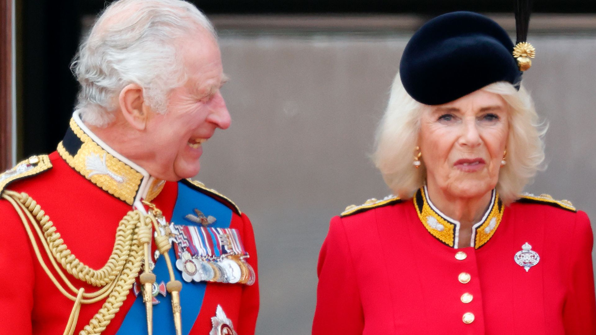 King Charles III and Queen Camilla wearing red outfits on the balcony at Buckingham Palace