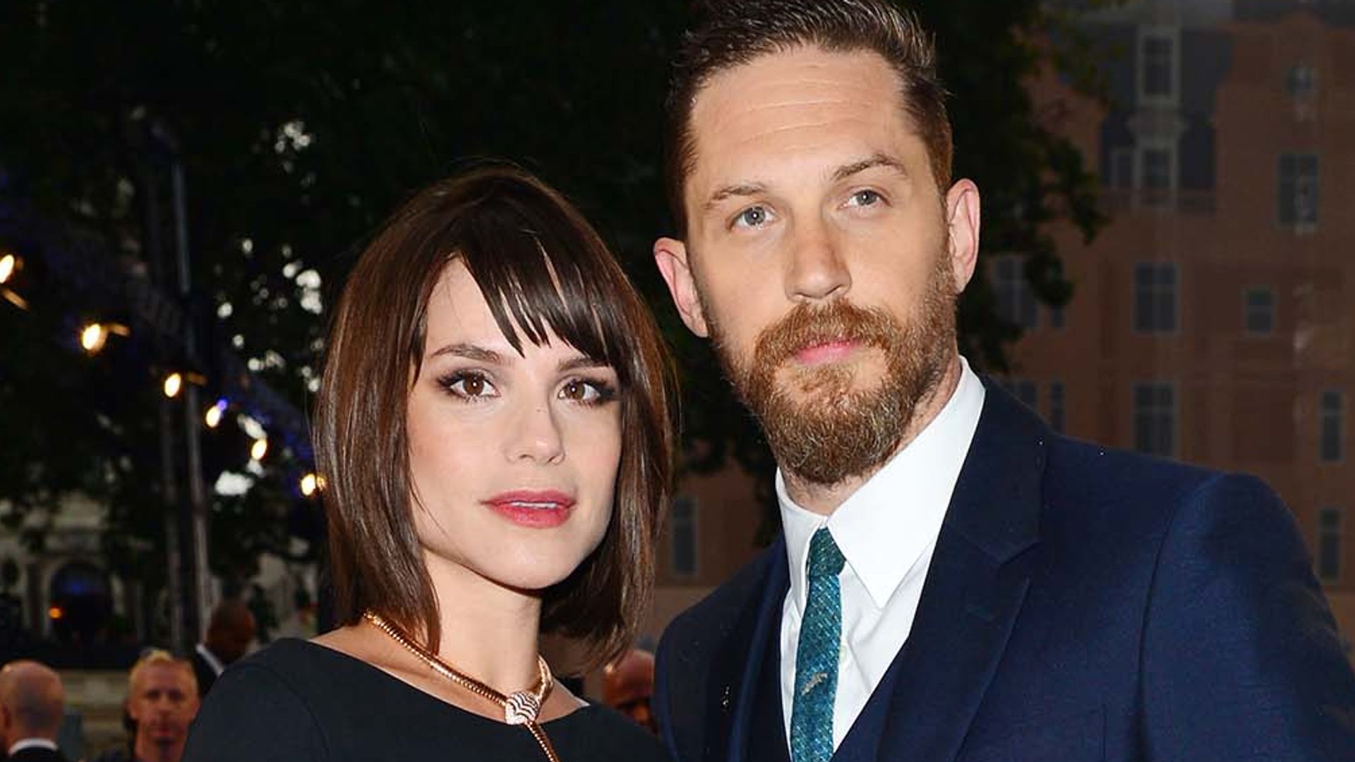 Tom Hardy in a blue suit on the blue carpet with wife Charlotte Riley