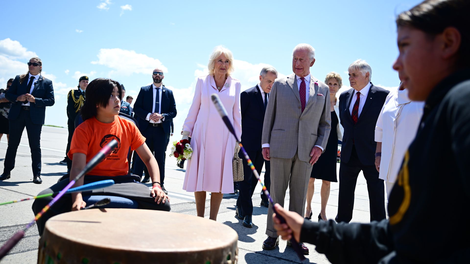 King Charles and Queen Camilla watching two children playing drums