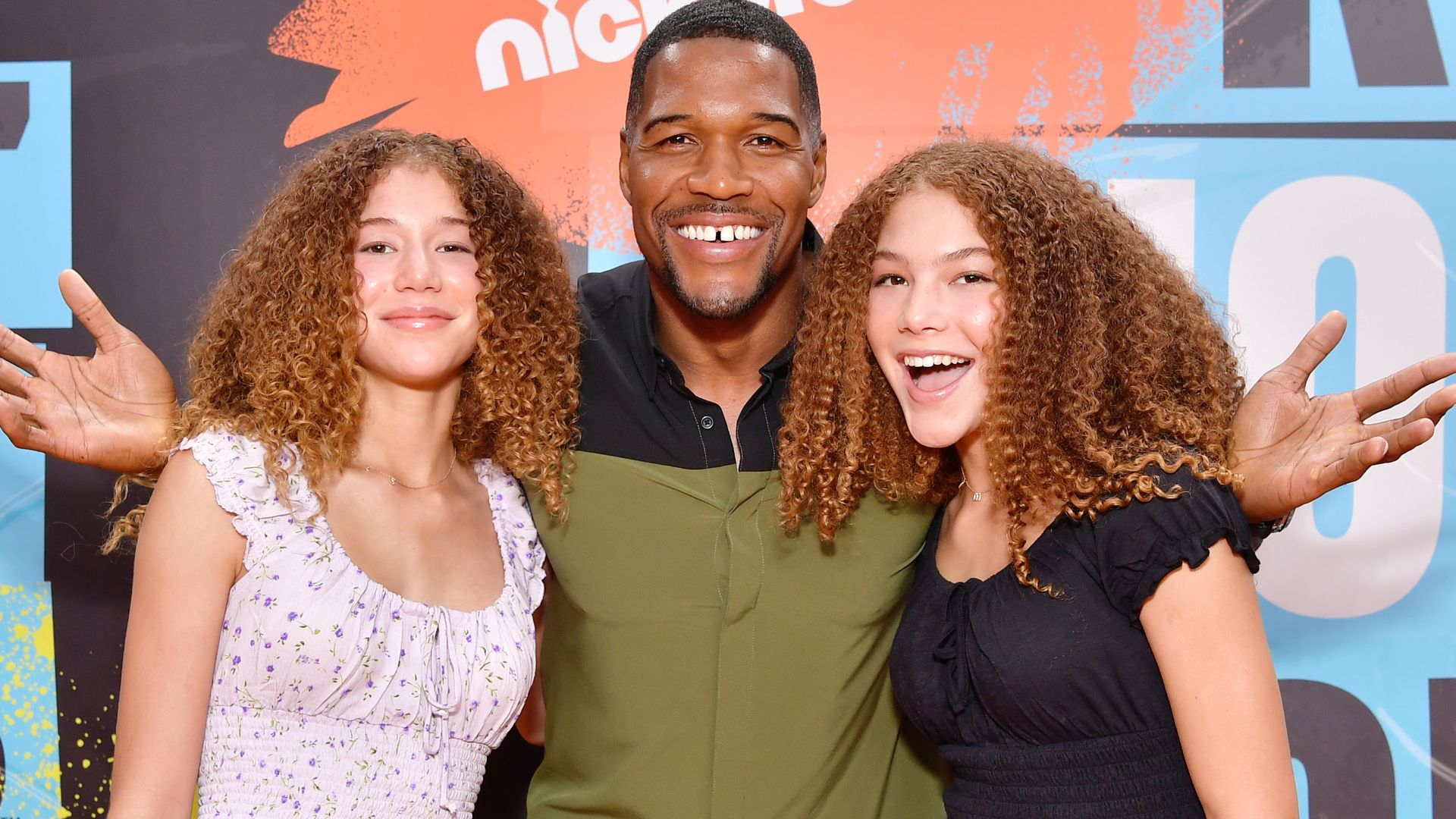 Michael Strahan with his twin daughters Sophia and Isabella smiling on a red carpet