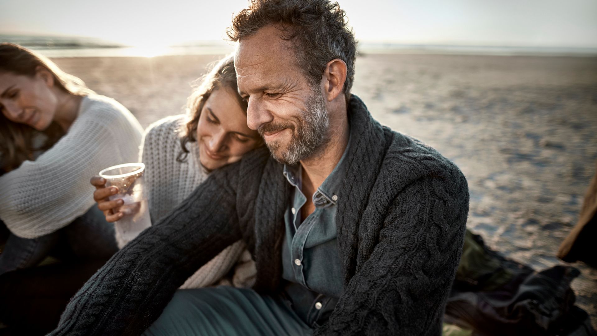 Woman leaning against man's shoulder on the beach at sunset
