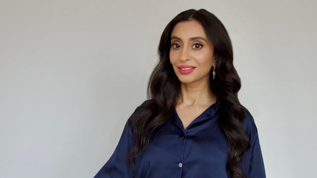 Woman in a blue silky blouse and white trousers smiling 