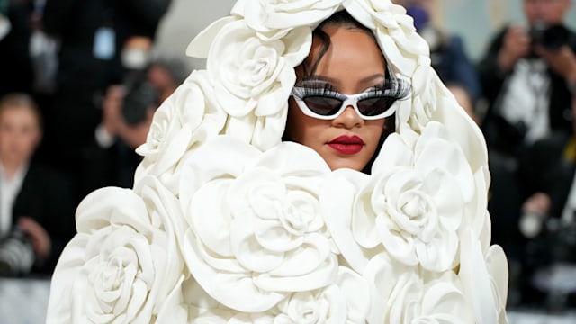 Rihanna attends the 2023 Met Gala in a rose adorned white cape and white sunglasses with false lashes