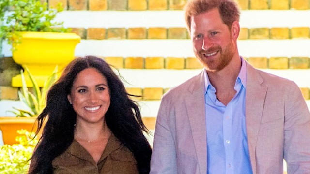 Meghan Markle smiling in a green dress with her husband Prince Harry