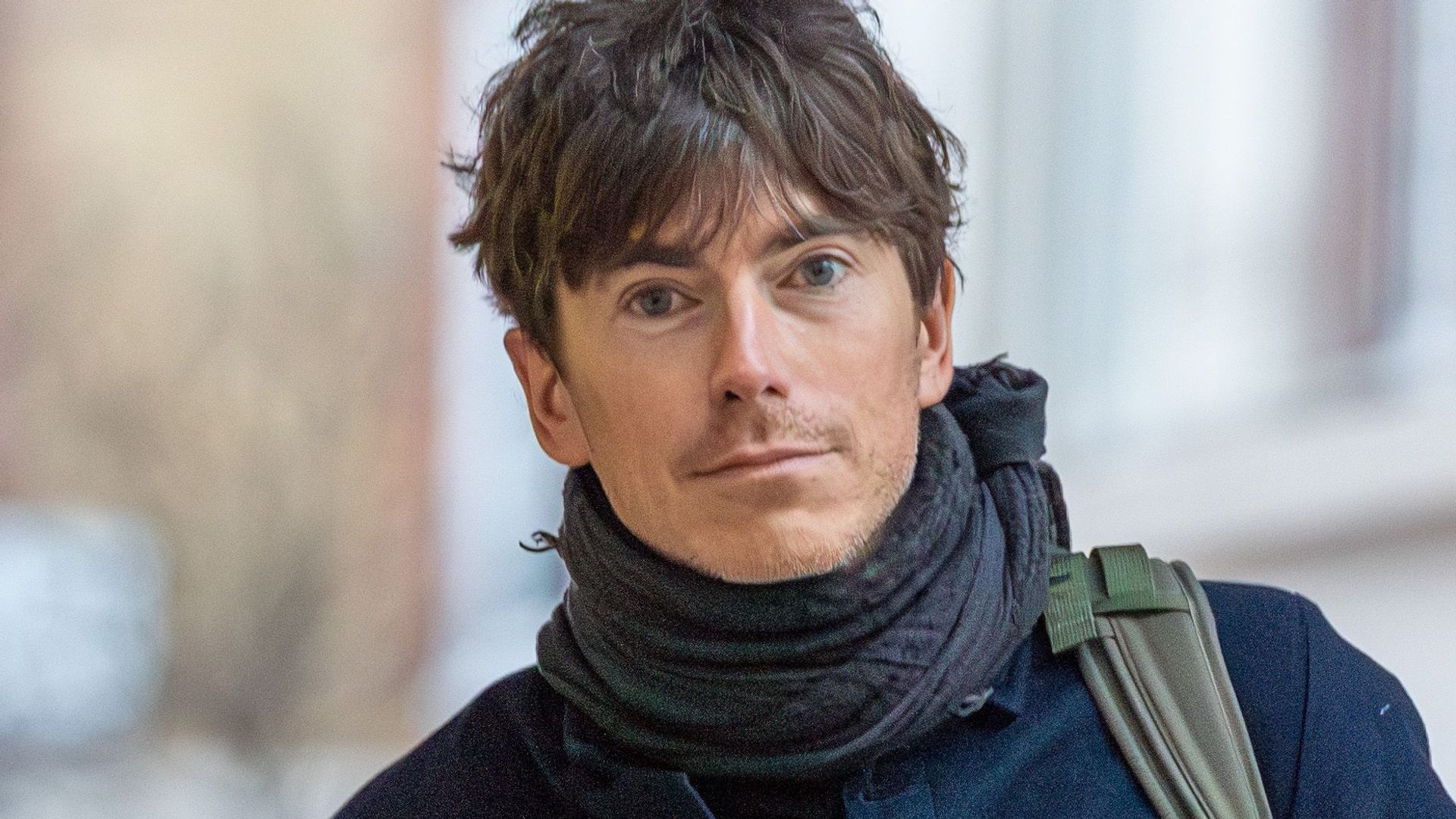Simon Reeve in a blue coat and scarf walking down a street