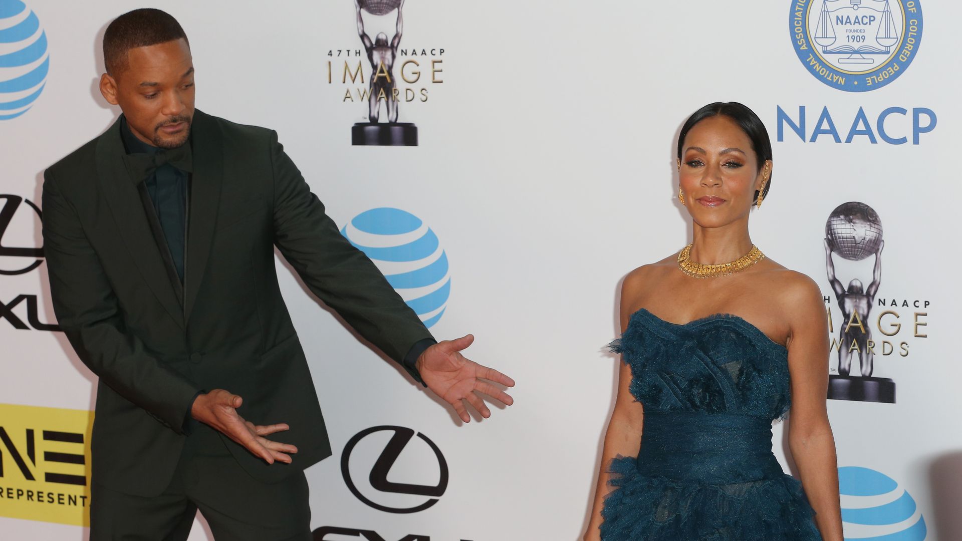 Will Smith and Jada Pinkett Smith at a red carpet event, Will is celebrating his wife by stepping to the side and pointing at her