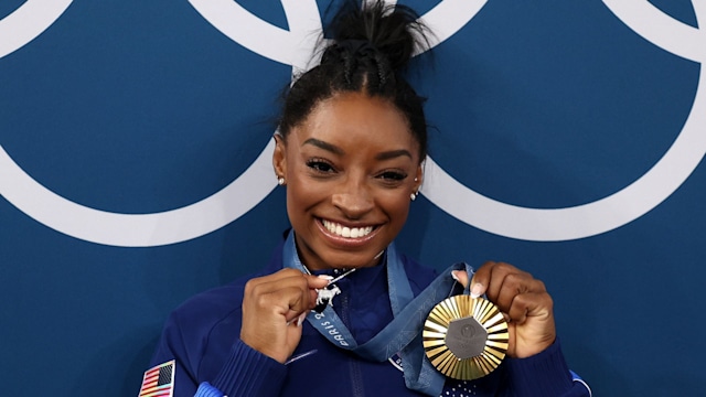 Gold medalist Simone Biles of Team United States poses with the Olympic Rings and a goat charm on her necklace during the Artistic Gymnastics Women's All-Around Final medal ceremony on day six of the Olympic Games Paris 2024 at Bercy Arena on August 01, 2024 in Paris, France.