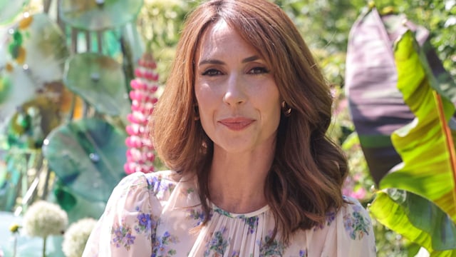 Alex Jones in a floral dress in front of greenery