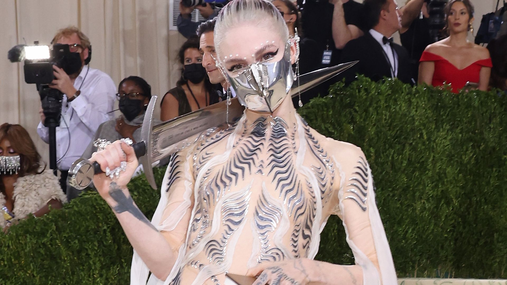 Grimes at the Met Gala 2021 wearing a metal mask and holding a sword on her shoulder