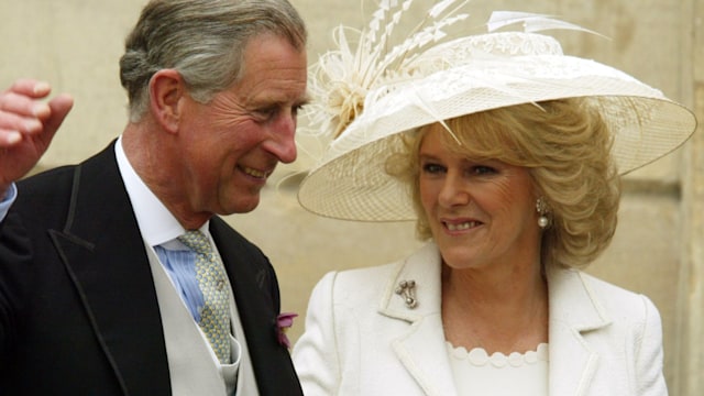 King Charles waving while Queen Camilla looks on in a white dress
