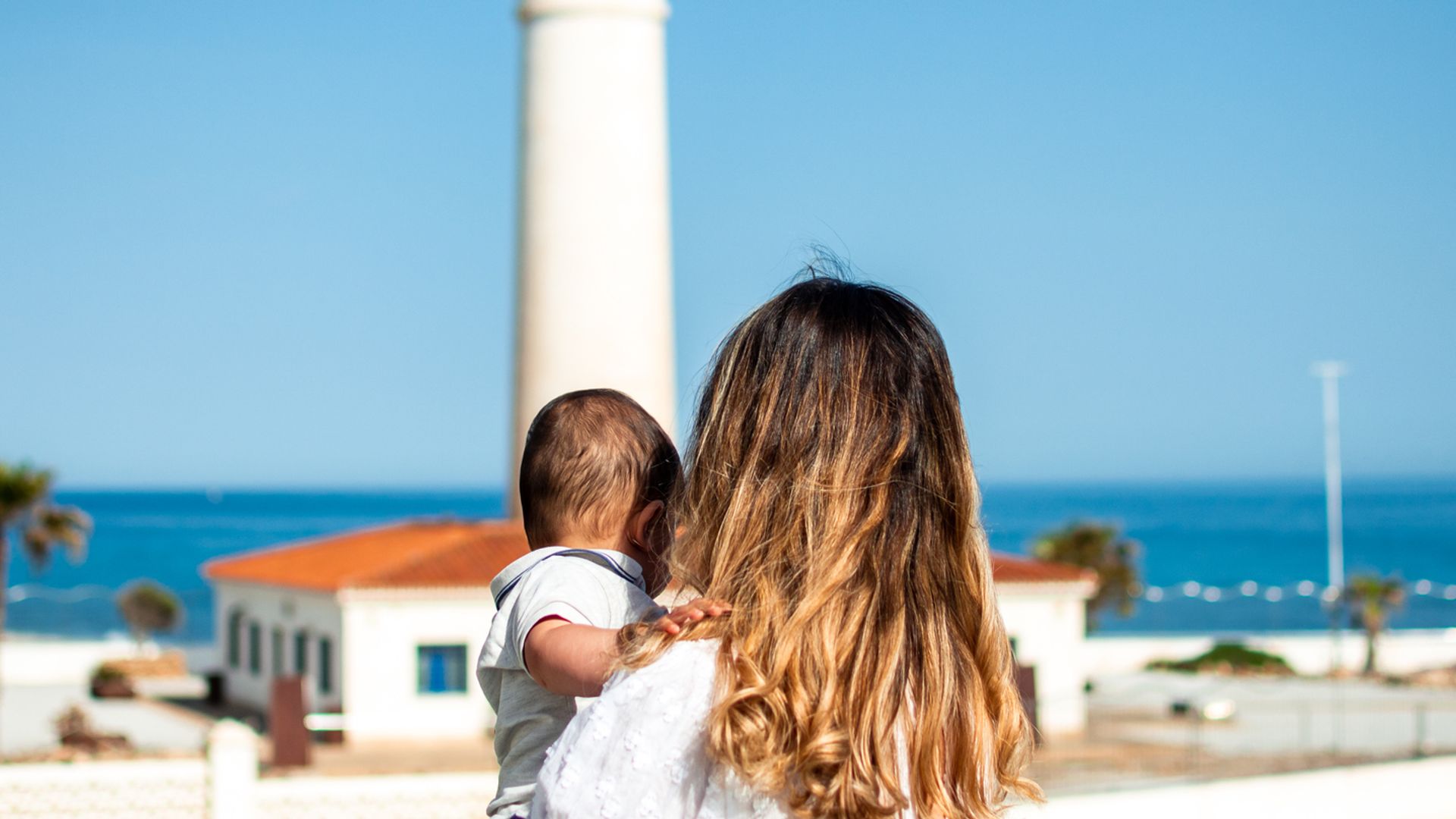 Mother and baby gazing at a coastal landscape and lighthouse.