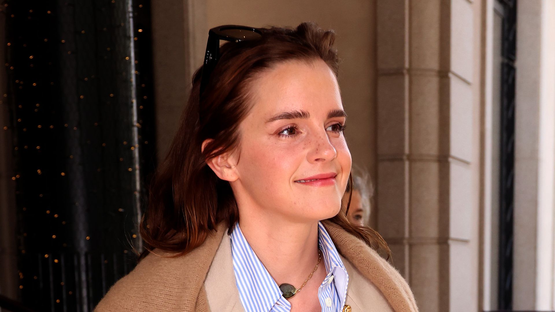 Emma Watson in a trench coat and blue jeans walking in the sunlight