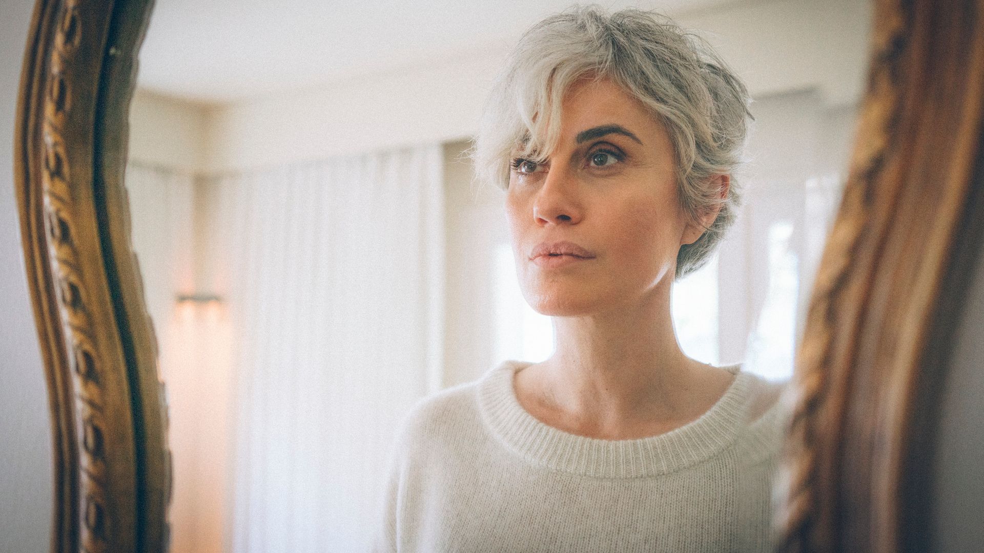 An ageless, short-haired woman examines herseÅf by the mirror