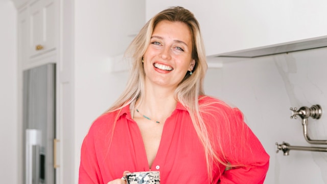 Woman in pink shirt in a white kitchen drinking tea 