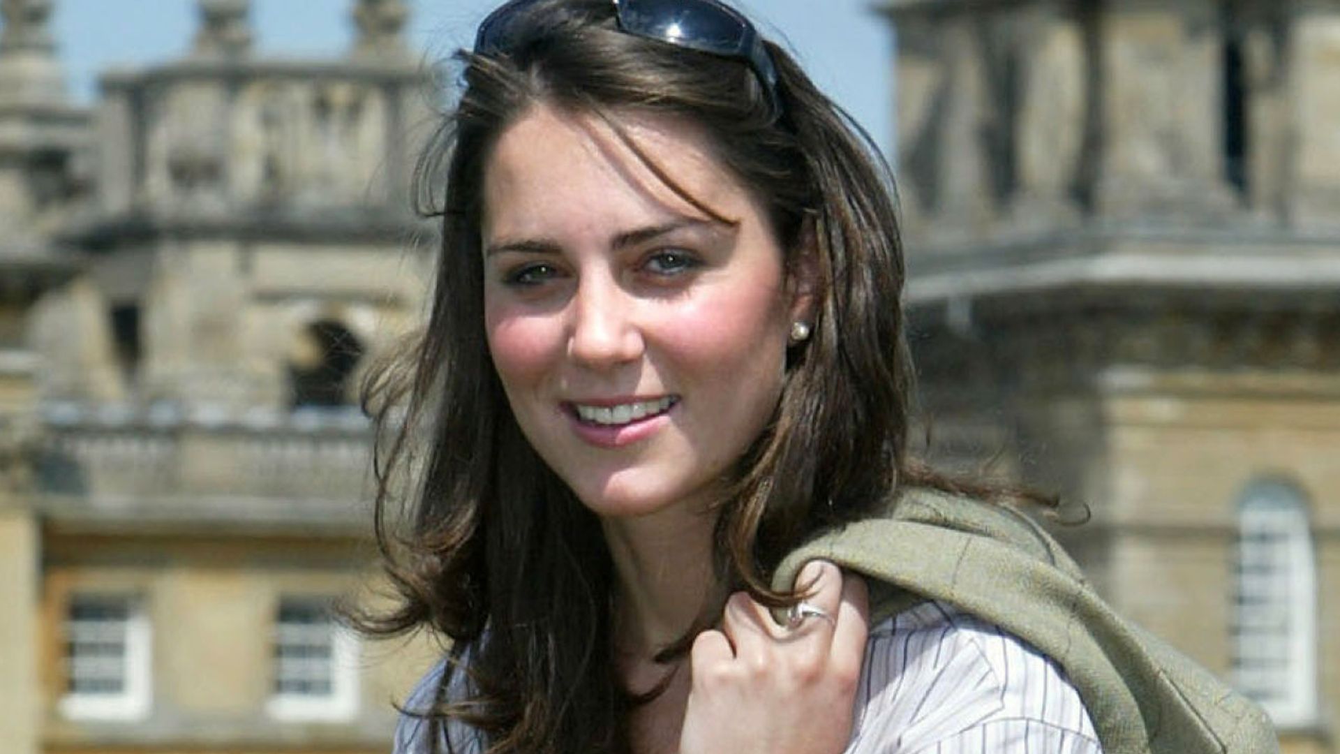 Kate Middleton holding a jacket in front of a palace