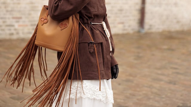 Pornwika Spiecker wears long white skirt, brown jacket, dusty pink turban, sunglasses and brown bag outside the Munthe fashion show
