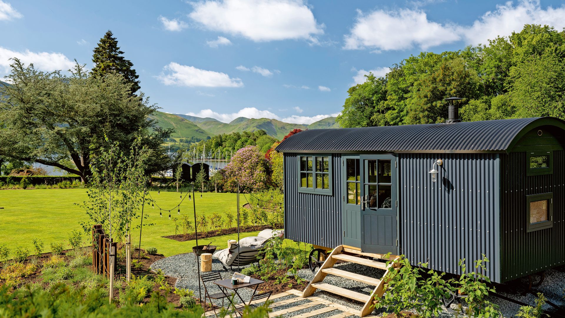 Countryside shepherd's hut with a landscaped garden, outdoor seating, and scenic hills in the background.