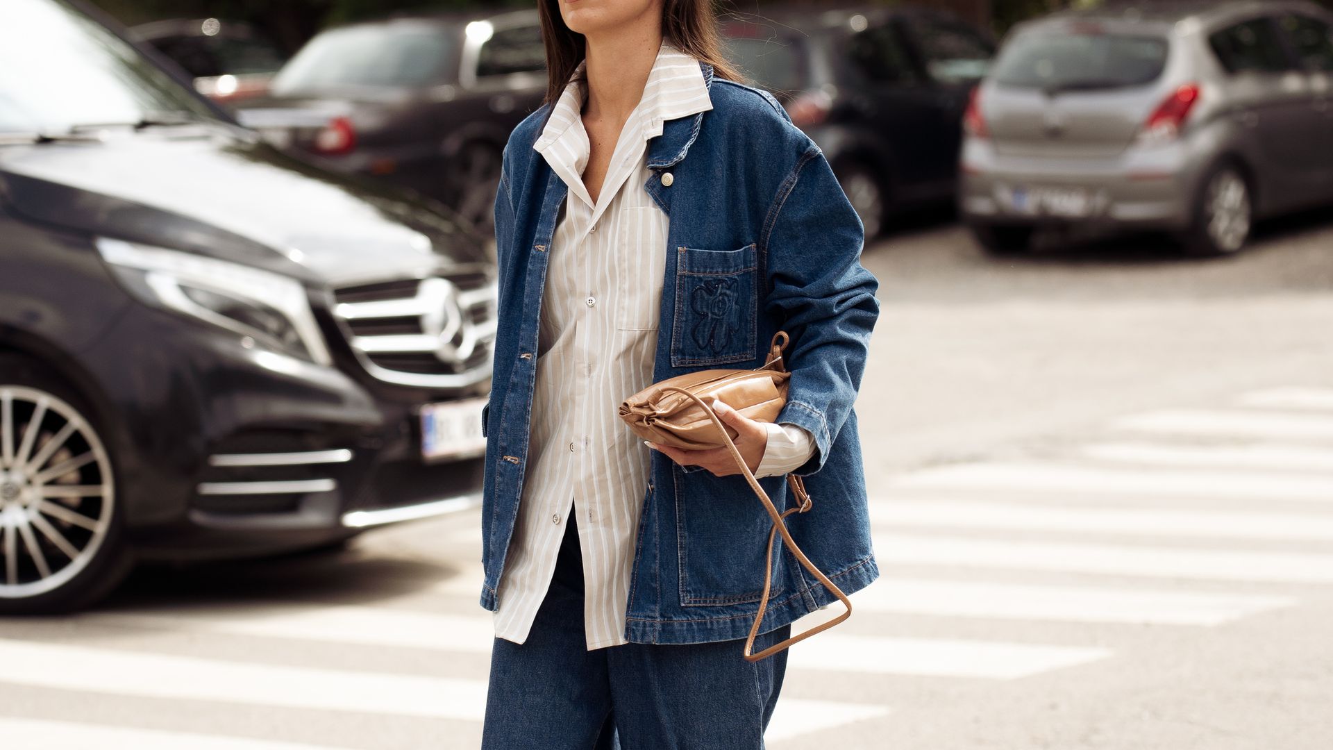 A gueast wears blue wide jeans, white shirt, blue shirt and brown bag outside Marimekko show during Copenhagen Fashion Week day four on August 07, 2025 
