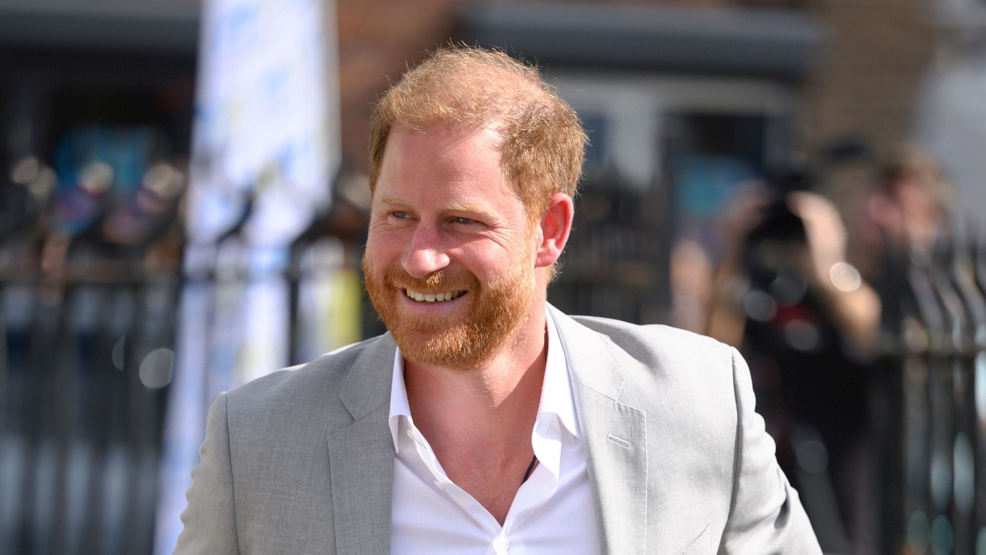 Prince Harry smiling in white shirt and grey blazer