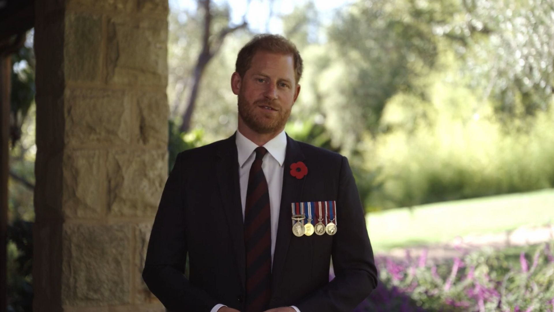 Prince Harry wearing a black suit and military medals inside Montecito home