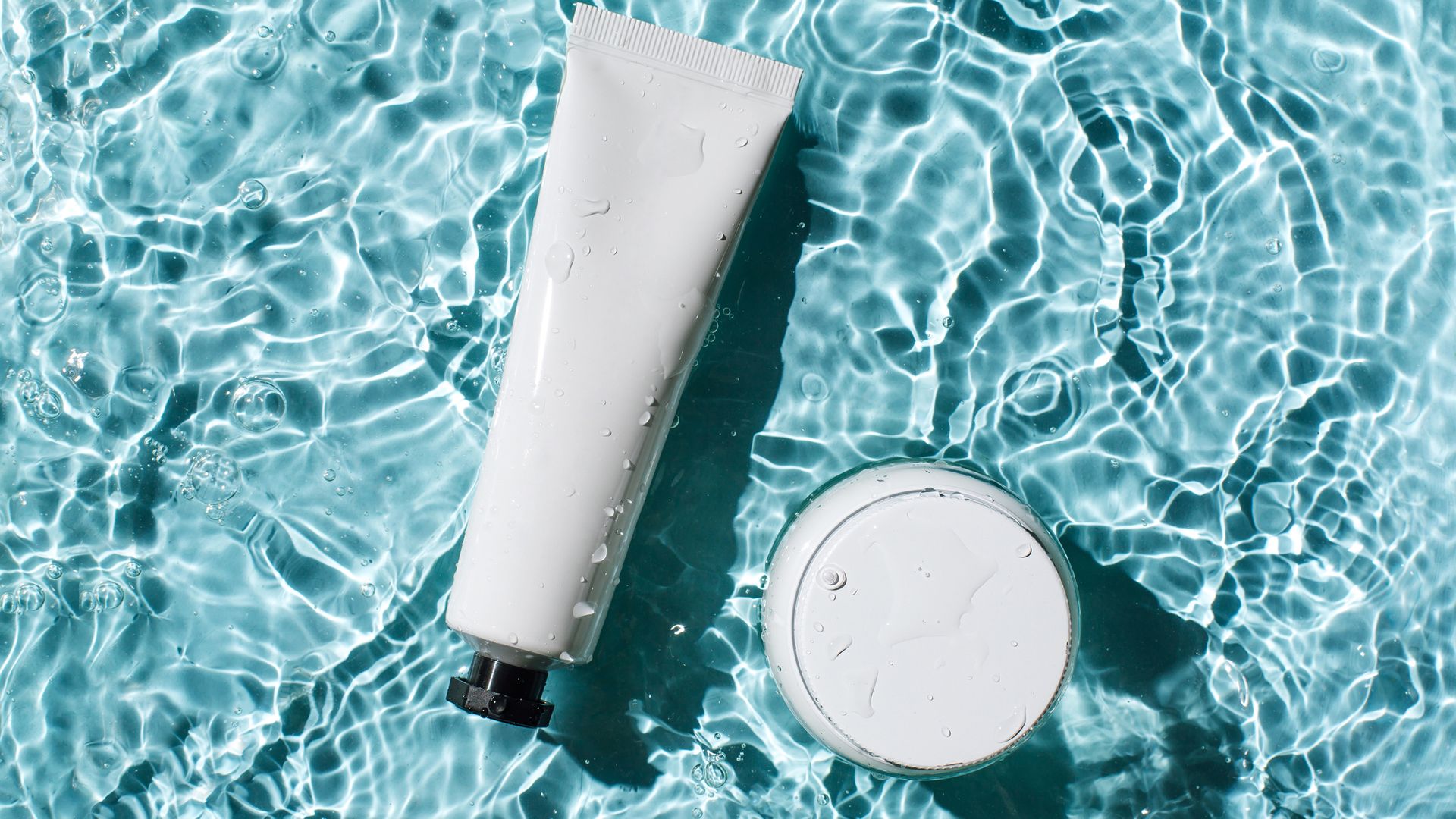 Bottles of natural cosmetics with sunscreen against sunburn on the background of blue water with waves. Beauty products for body and face care.