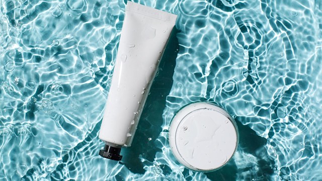 Bottles of natural cosmetics with sunscreen against sunburn on the background of blue water with waves. Beauty products for body and face care.