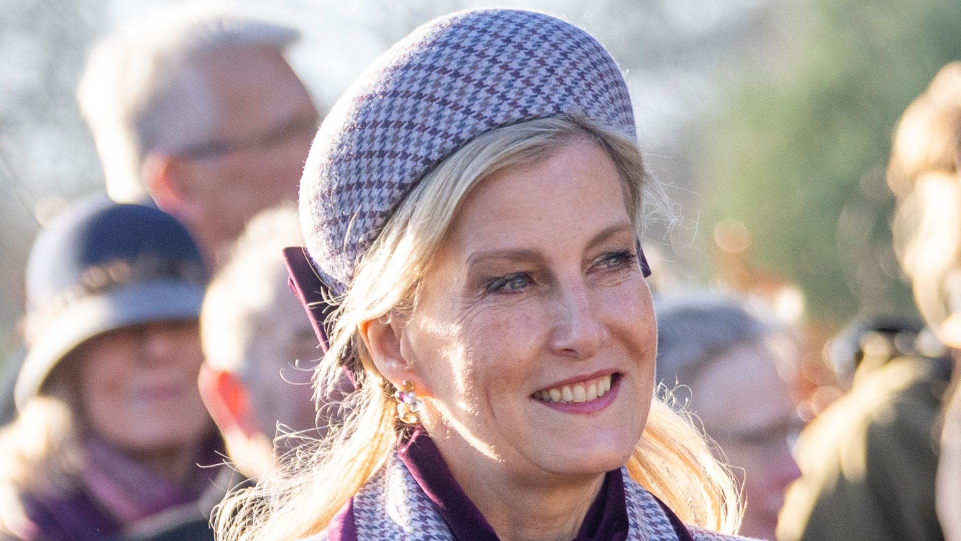 Sophie, Duchess of Edinburgh wearing houndstooth hat and coat holding flowers and smiling
