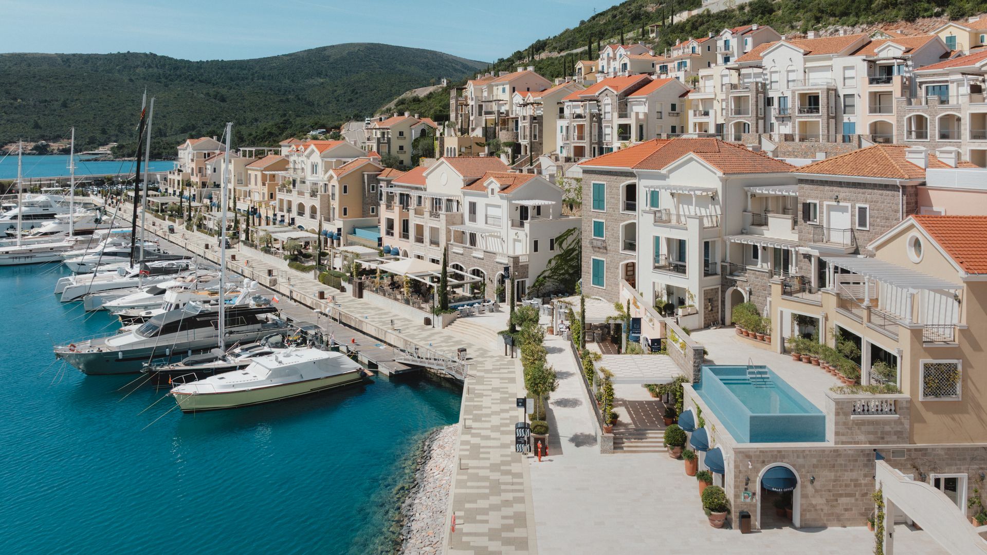 An aerial view captures Lustica Bay, Montenegro, featuring a marina filled with yachts alongside a stone promenade.